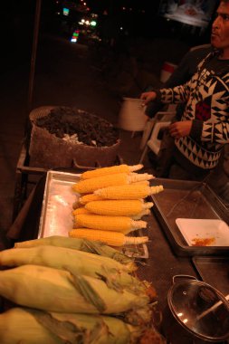 Geceleri mısır satan bir sokak satıcısı, arka planda ızgara mısır ve ön planda taze mısır.