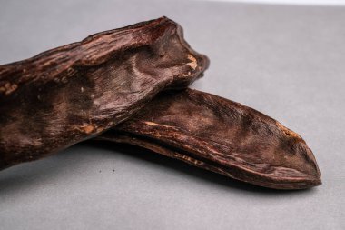 Tarafsız Gri Arkaplanda Geçiş yapan İki Kurutulmuş Keçiboynuzu (Ceratonia silika) Macro Still Life of Two Kurutulmuş Keçiboynuzu.