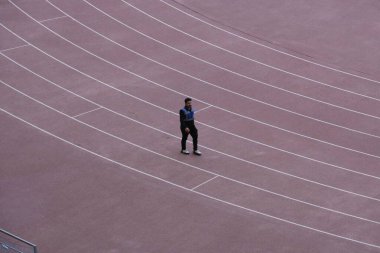 Boş bir stadyumda koşu pistinde yürüyen yalnız bir sporcu.