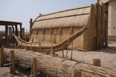 Sazlık ve bambudan yapılmış geleneksel bir yapı, yakınındaki kumlu bir alana kurulmuş teknesi olan bir evi andırıyor.