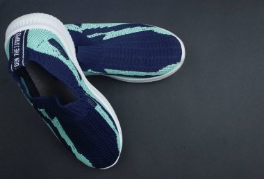 Lacivert ve nane yeşili renklerde, örülmüş üst ve beyaz tabanlı koyu bir arka plana yerleştirilmiş bir çift modern kaygan spor ayakkabı.