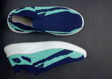 Lacivert ve nane yeşili renklerde, örülmüş üst ve beyaz tabanlı koyu bir arka plana yerleştirilmiş bir çift modern kaygan spor ayakkabı.