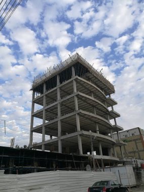 Bulutlu bir gökyüzünün altında beton iskeleti ve iskelesi olan kısmen inşa edilmiş bir bina