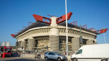 Eşsiz bir mimari tasarıma sahip modern bir spor stadyumu, üzerinde büyük kırmızı yapılar ve açık mavi gökyüzüne karşı beton bir taban yer alıyor.