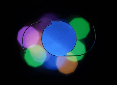 İnce çerçeveli dairesel bir lens, yeşil, mavi ve mor renkli bokeh lambaların arka planına yerleştirilmiş.