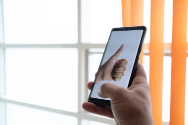 Elinde akıllı bir telefon olan ve arka planda parlak turuncu perdeleri olan bir insan.