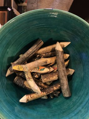 El yapımı ahşap kalemler boyalı yüzleri ve çiçekleri seramik bir kaseye yerleştirilmiş, tepeden tırnağa manzaralı kazınmış sopalar.