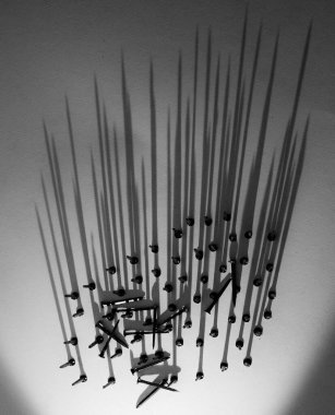 Dağınık vidaların siyah ve beyaz fotoğrafı dokulu bir yüzeyde uzun dikey gölgeler oluşturuyor, çarpıcı yüksek kontrastlı ışıklandırma.