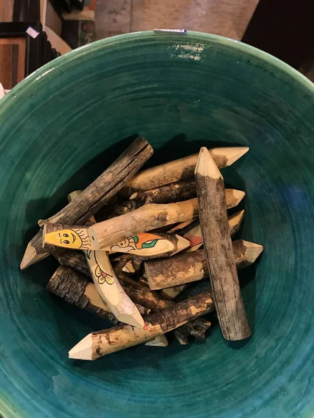 El yapımı ahşap kalemler boyalı yüzleri ve çiçekleri seramik bir kaseye yerleştirilmiş, tepeden tırnağa manzaralı kazınmış sopalar.