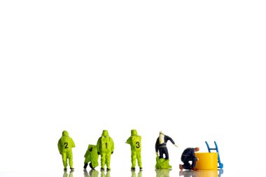 Büyük korona virüsünün, gaz ve diğer kimyasal kazalar sırasında müdahale eden özel tıbbi güçlerden oluşan minyatür figürlerle yakın plan çekimleri, beyaz zemin üzerinde çok tehlikeli ölümcül virüs türüne karşı teşhis ve eyleme hazırlanan ekip 