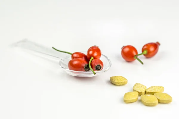 Rose hip on a medicine spoon with vitamine pills — Stock Photo, Image