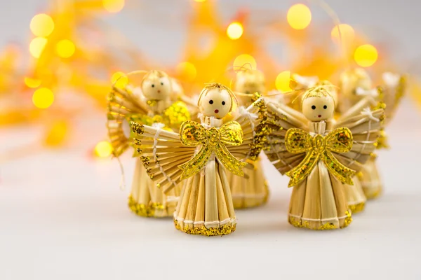 Sechs Weihnachtsengel aus Stroh auf weißem Hintergrund mit verschwommenem gelben Weihnachtslicht — Stockfoto