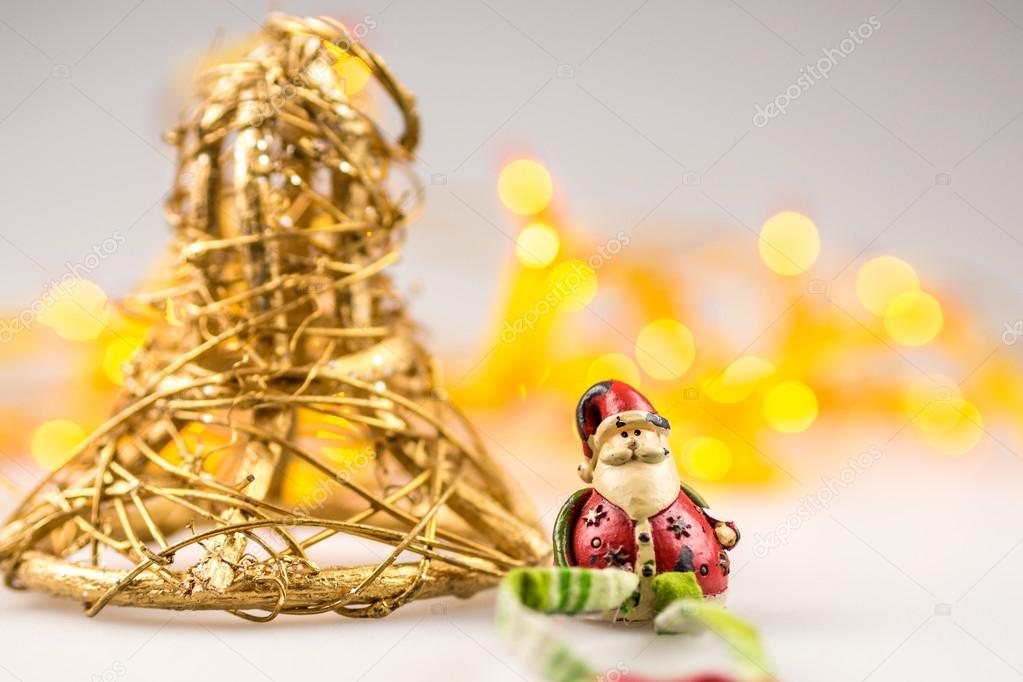 One straw christmas bell and oneceramic santa claus on white background with blurred yellow christmas lights