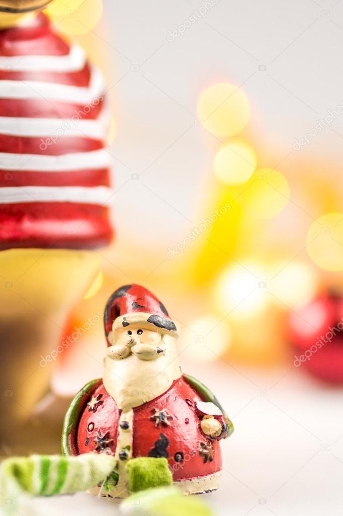 One ceramic christmas reindeer and one ceramic santa claus on white background with blurred yellow christmas lights