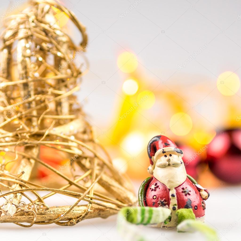 One straw christmas bell and one ceramic santa claus on white background with blurred yellow christmas lights