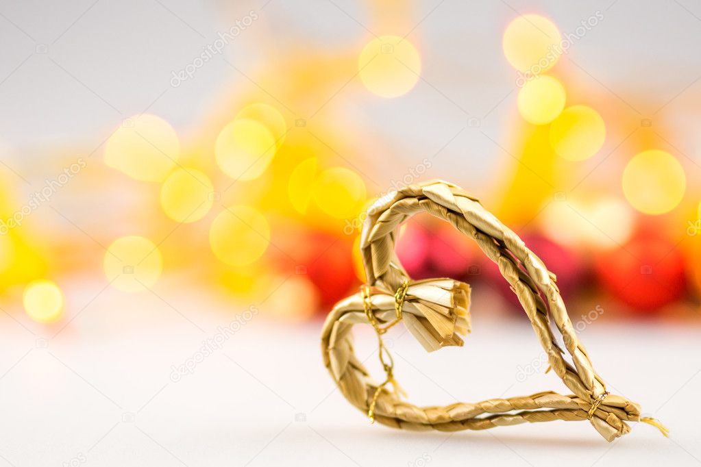 One straw christmas heart on white background with blurred yellow christmas lights
