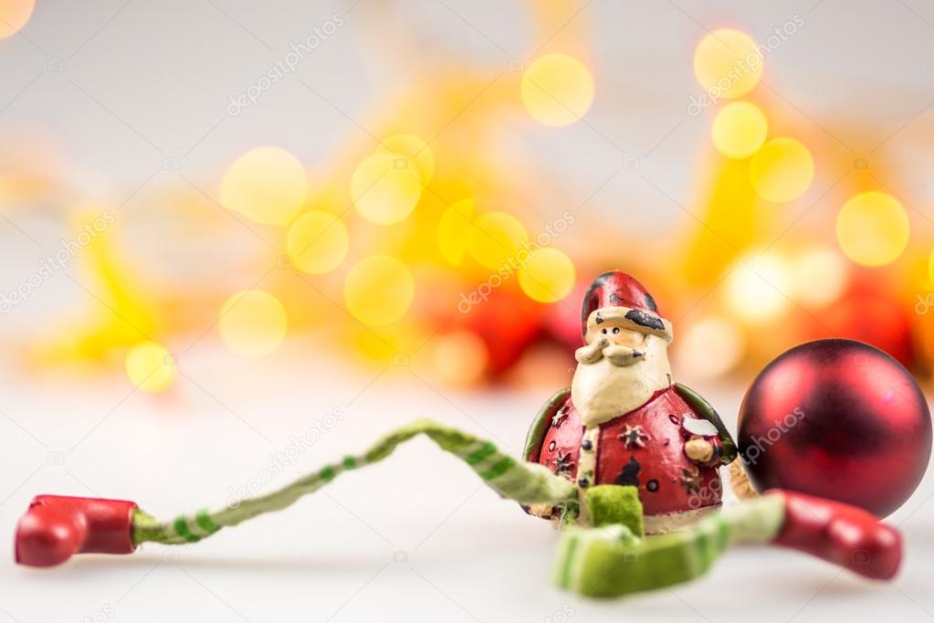 One ceramic santa claus and one red christmas ball on white background with blurred yellow christmas lights