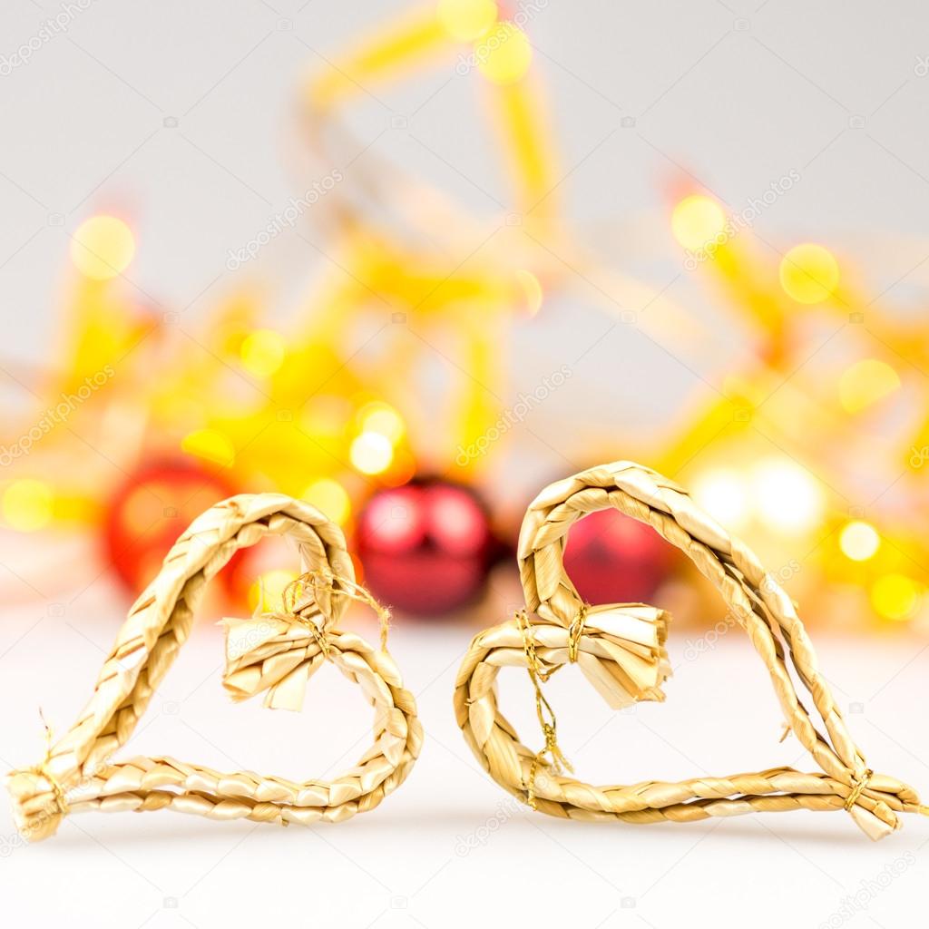 Two straw christmas hearts on white background with blurred yellow christmas lights