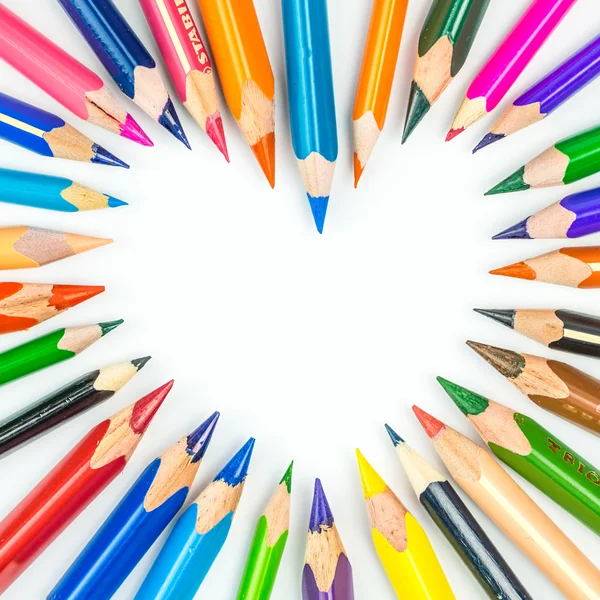 Spousta různých a barevné tužky tvoří srdce na bílém pozadí — Stock fotografie
