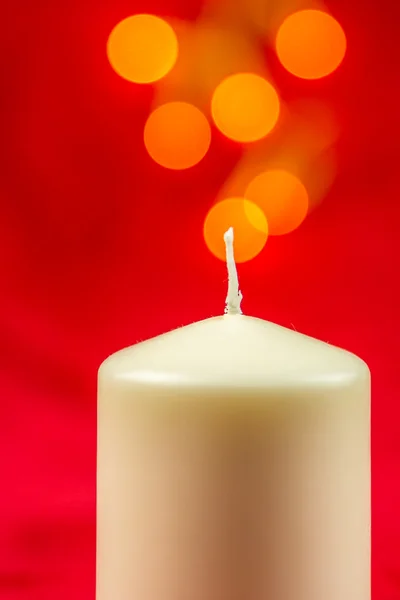 White christmas wax candle on red background with bright yellow lights — Stock Photo, Image