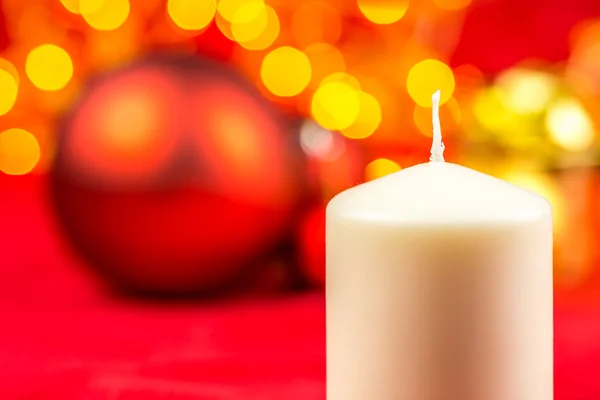Біла різдвяна воскова свічка та кульки на червоному тлі з яскравими жовтими вогнями — стокове фото