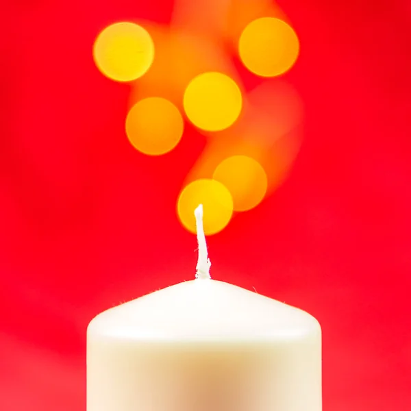 Біла різдвяна воскова свічка на червоному тлі з яскравими жовтими вогнями — стокове фото