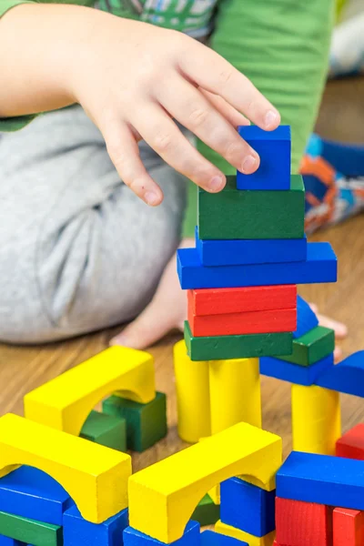 Child is playing with multicolored cubes on wooden floor — Stock Photo, Image