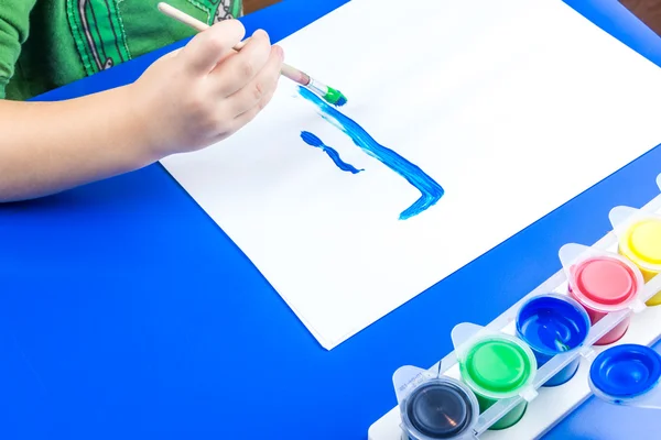 Niño está pintando un cuadro con pinturas de tempera en la mesa azul —  Fotos de Stock