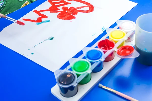 Niño está pintando un cuadro con pinturas de tempera en la mesa azul —  Fotos de Stock