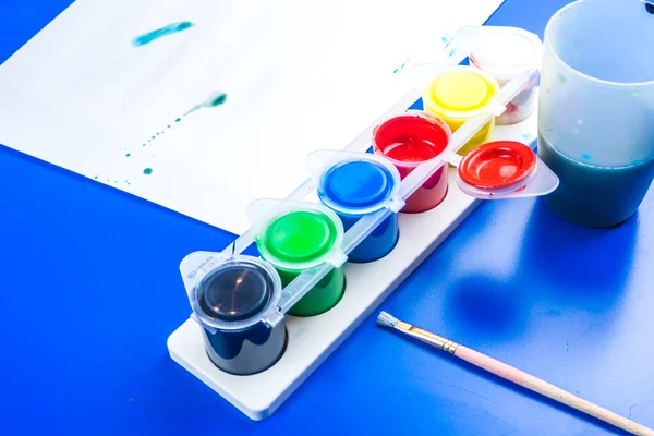 Ребенок рисует картину темпера красками на синем столе — стоковое фото