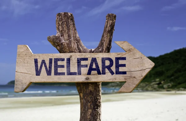 Welfare segno di legno con una spiaggia sullo sfondo — Foto Stock