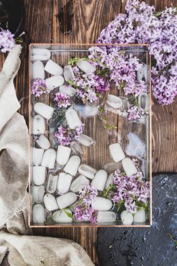 Tahta arka planda buz parçaları ve leylak çiçekleri olan yaz tepsisi