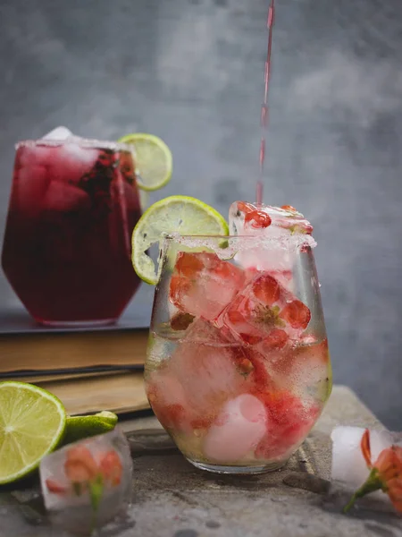 A glass with ice cubes and a pink drink