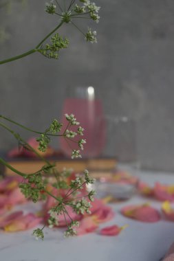 Gül yapraklı pembe kokteyl ve gri arka planda buz küpleri.