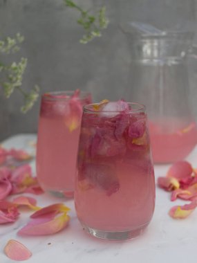 Gül yapraklı pembe kokteyl ve gri arka planda buz küpleri.