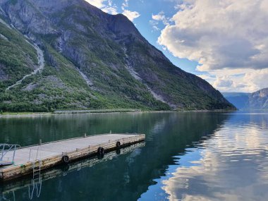 Gökyüzünün yansımasında iskele ve fiyordun mavi suyunda dağlar - Eidfjord
