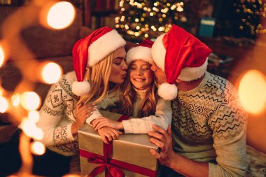 Mutlu Noeller ve mutlu yıllar! Mutlu aile Noel Baba 'nın yeni yılını bekliyor. Şapkalar birbirine hediye veriyor. Anne ve baba tatlı bir kızı öpüyor.