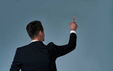 A young man with his back turned to camera, pointing to something. Businessman executive pointing up.