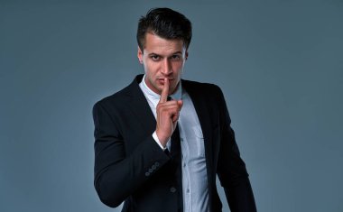 Young handsome businessman wearing elegant suit standing over isolated gray background asking to be quiet with finger on lips. Silence and secret concept.