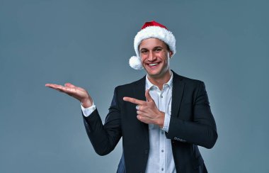 Business man in christmas hat holding copy empty blank space on  palms advert sale discount isolated over on a gray background and smiling.