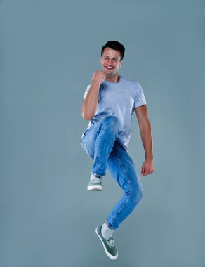Full length portrait of an excited young man in gray t-shirt jumping while celebrating success isolated over gray background.
