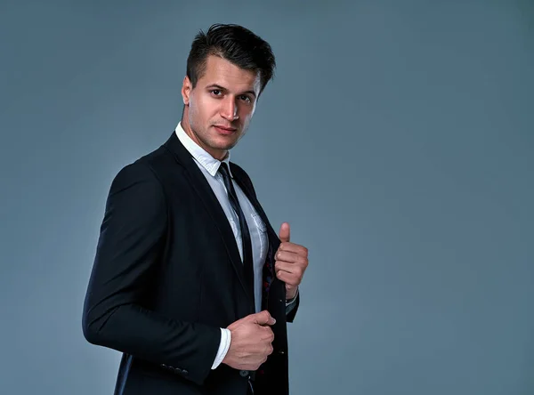 Handsome young brunette model, wearing in black and white suit, looking with attitude, posing at studio, isolated on gray background. Business man portrait. Copy space. Horizontal view.