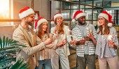 Veselé Vánoce a šťastný nový rok! Multiraciální mladí tvůrčí lidé slaví svátky s jiskry v moderní kanceláři. Skupina mladých podnikatelů pije šampaňské v prostoru pro spolupráci..