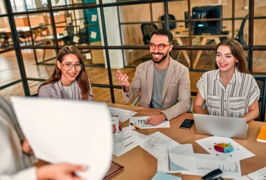 Cropped image of business woman showing graph on paper to group of colleagues sitting at table with laptops in modern office.