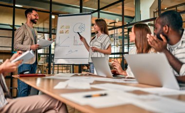 Genç bir grup iş adamı, yeni bir iş planını karatahtayla tartışıyor. Modern bir ofiste otururken dizüstü bilgisayarlar üzerinde çalışıyorlar..