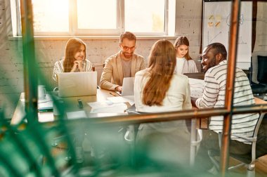 Genç profesyonel takım. Zarif gündelik giysiler içindeki bir grup modern insan yaratıcı ofiste cam duvarın arkasında otururken beyin fırtınası yapıyorlar.