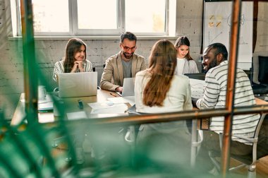 Genç profesyonel takım. Zarif gündelik giysiler içindeki bir grup modern insan yaratıcı ofiste cam duvarın arkasında otururken beyin fırtınası yapıyorlar.