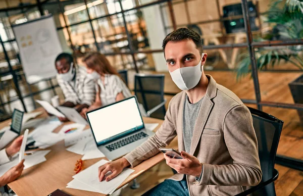 Young Caucasian Business Man Protective Mask Sits Laptop Holds Smartphone — Stock Photo, Image
