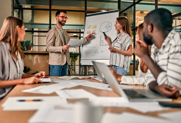 Genç bir grup iş adamı, yeni bir iş planını karatahtayla tartışıyor. Modern bir ofiste otururken dizüstü bilgisayarlar üzerinde çalışıyorlar..