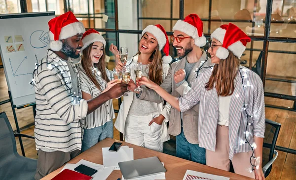 Mutlu Noeller ve mutlu yıllar! Çok ırklı genç yaratıcı insanlar modern ofiste bayramı kutluyorlar. Bir grup genç iş adamı birlikte çalışarak şampanya içiyor..